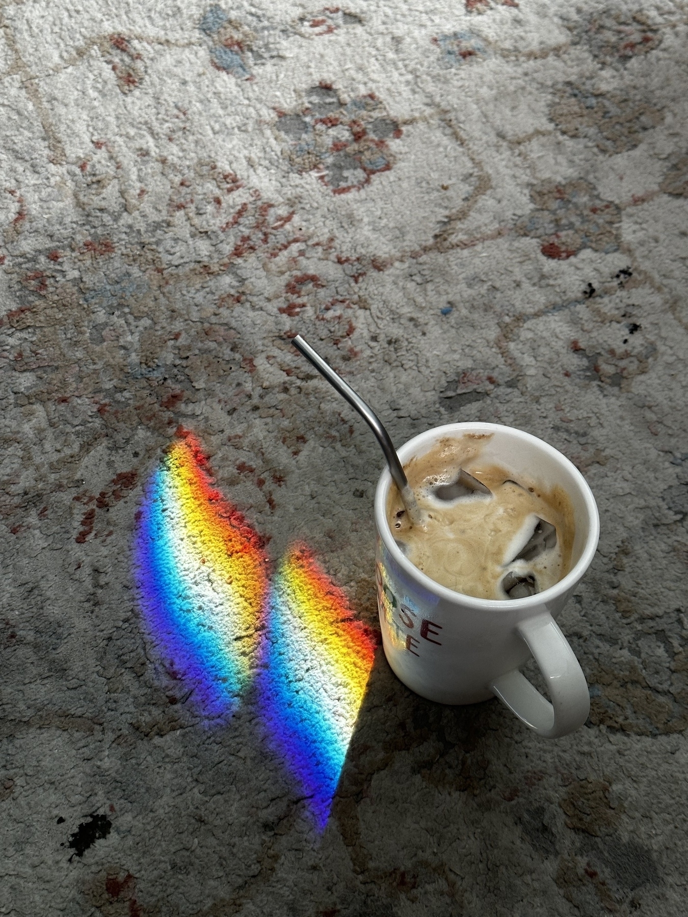 A coffee mug filled with coffee sitting next to a rainbow refracted through the living room windows 