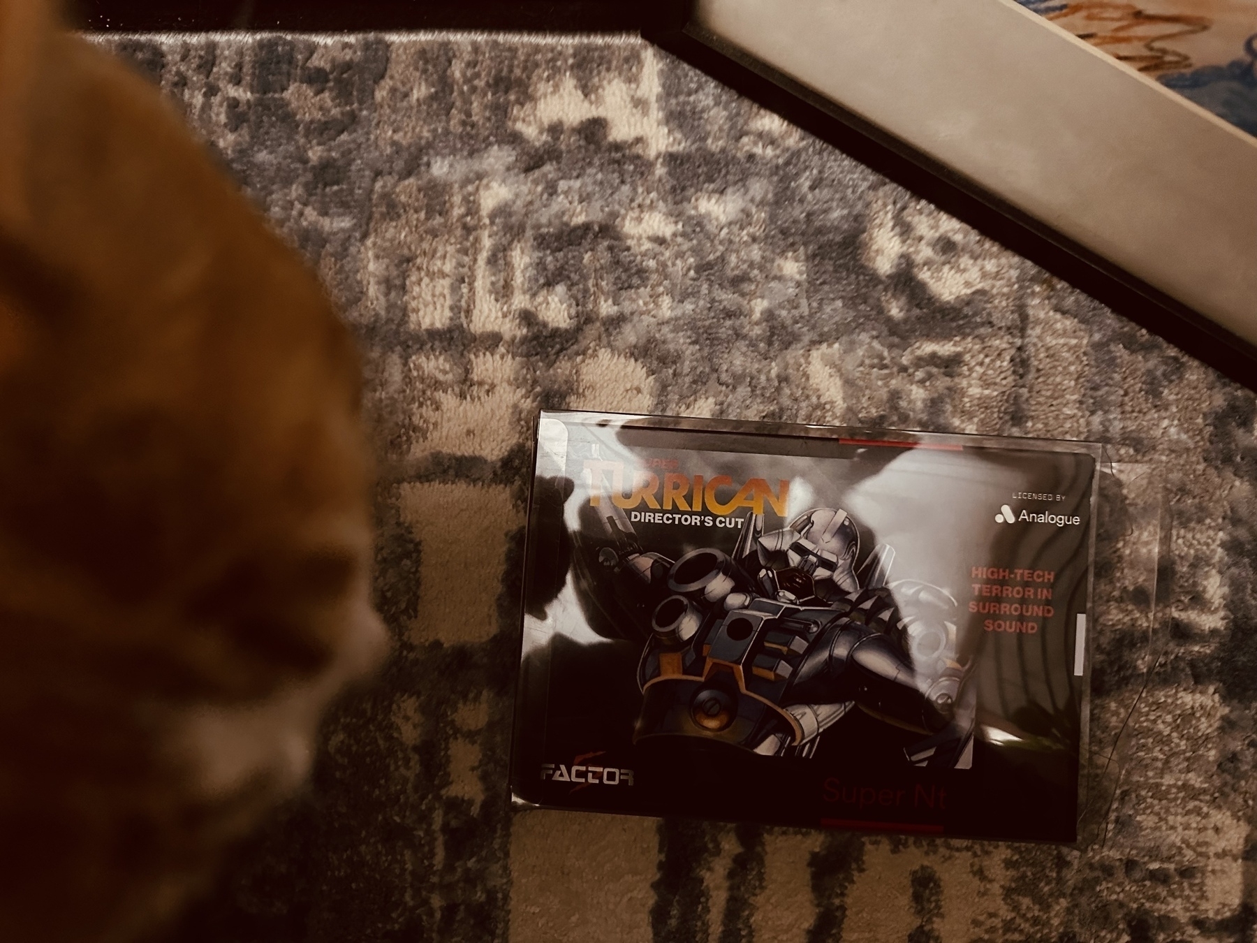 The box of Suoer Turrican: Director’s Cut, with a cat visible to the left and a painting to the right 