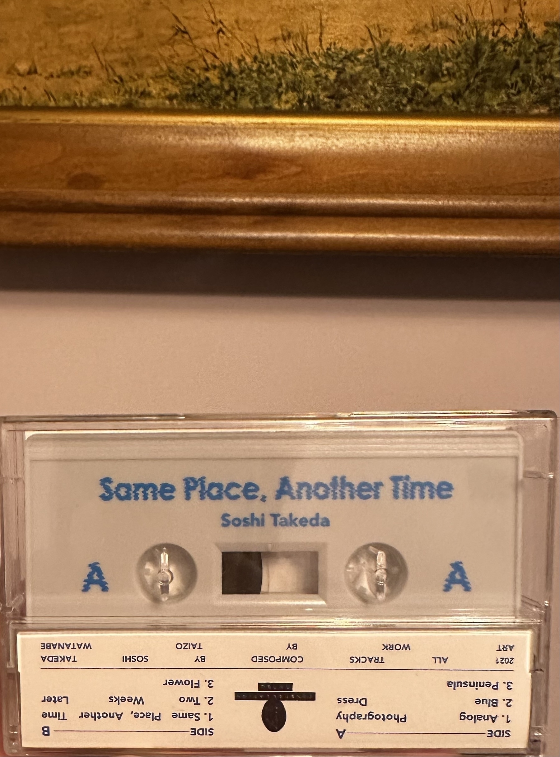 White cassette of Same Place, Another Time by Soshi Takeda. A painting is visible above it 
